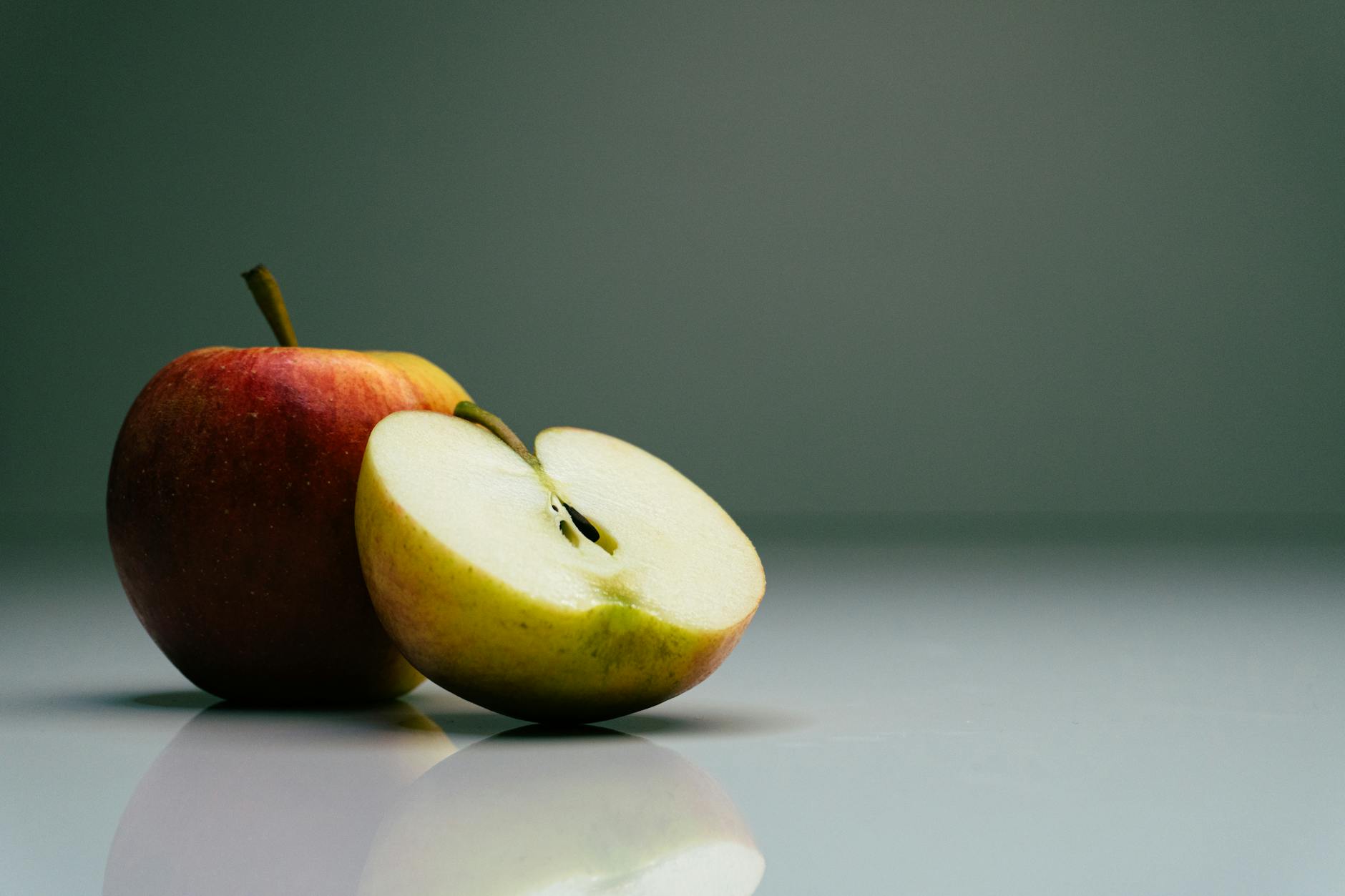 Close-up of a whole and sliced organic apple on a reflective surface.