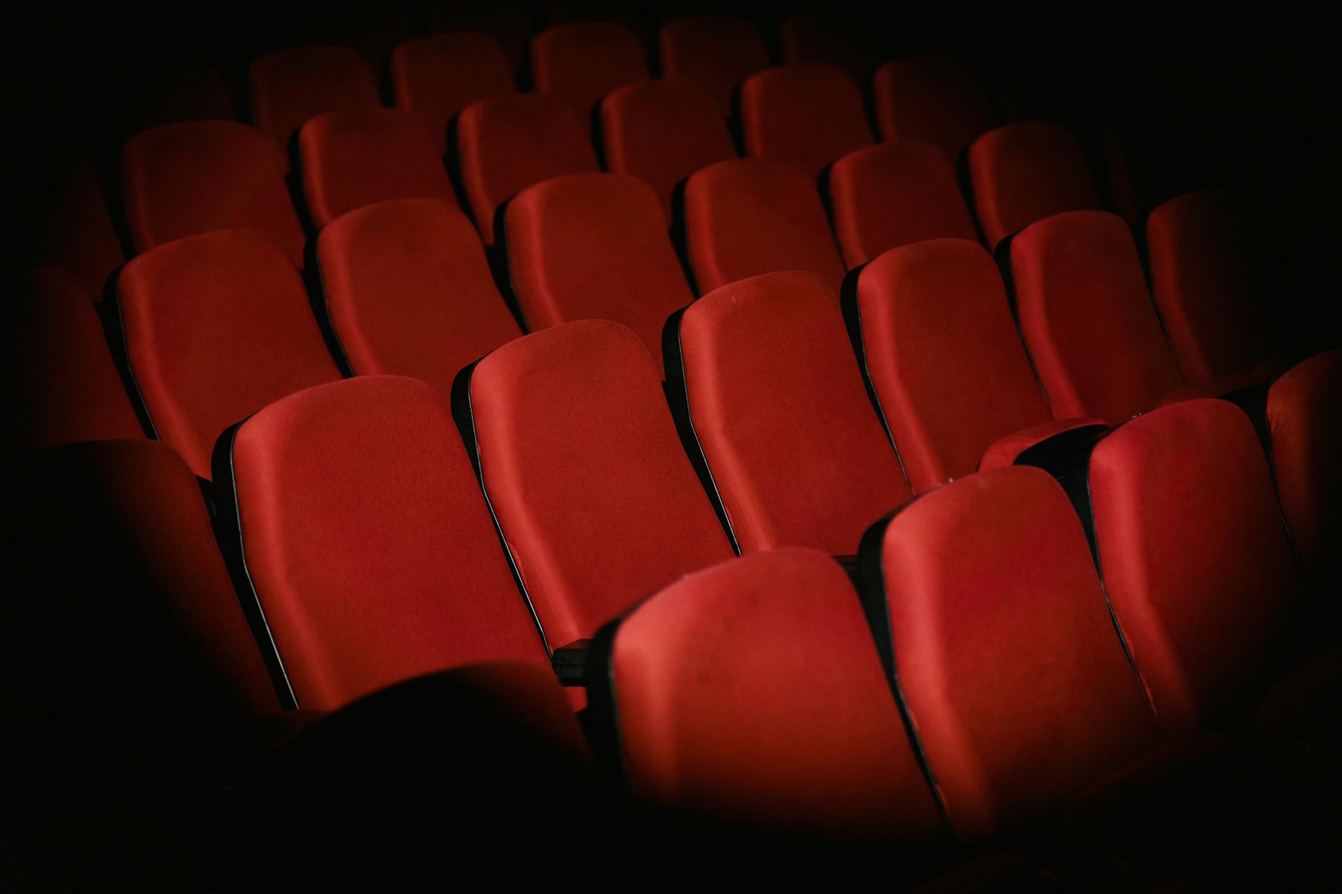 Rows of empty red armchairs in a dimly lit cinema setting, creating a moody atmosphere.