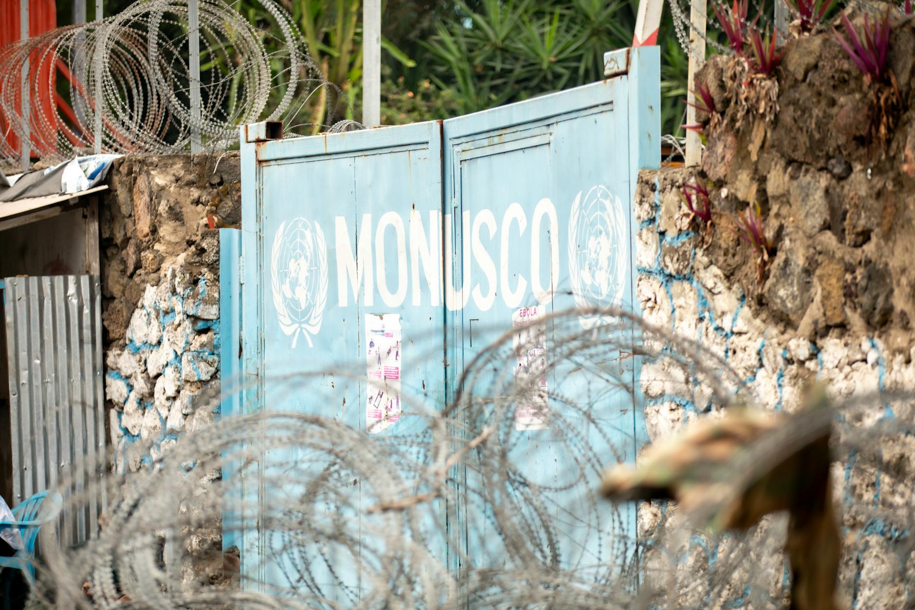 Barbed wire protecting the MONUSCO gate, surrounded by stone walls and plants.